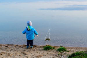 child at the sand beach near the water launched the little ship, the weather is cold, concept of disturbance