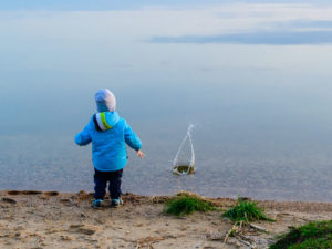 child at the sand beach near the water launched the little ship, the weather is cold, concept of disturbance