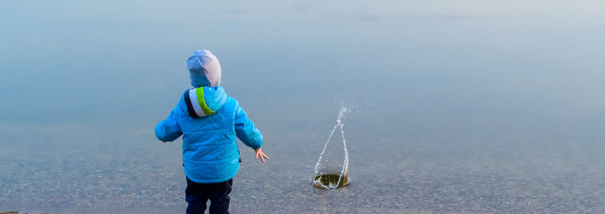 child at the sand beach near the water launched the little ship, the weather is cold, concept of disturbance