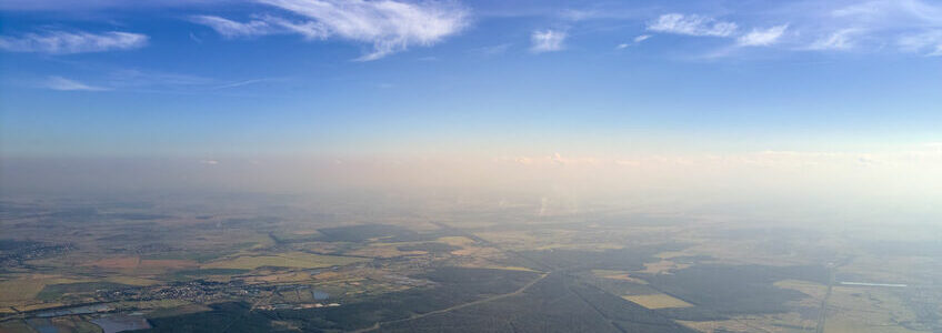 Aerial view of farm fields and distant scattered houses in rural area.